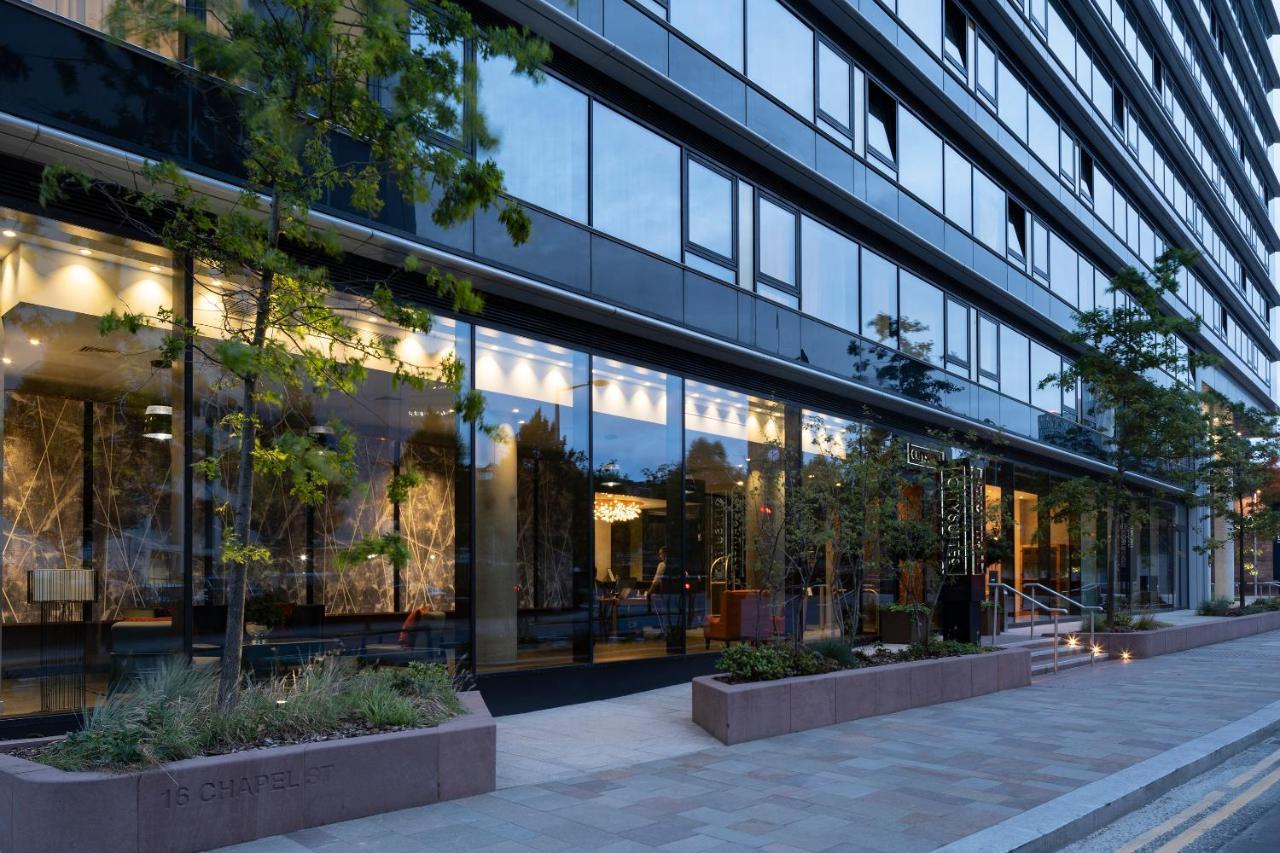 Citysuites Aparthotel Salford  Ngoại thất bức ảnh The photo shows a modern building with a glass facade, reflecting the surrounding environment. The structure has several floors and features large windows that allow visibility into the interior, which appears well-lit. There are trees and greenery p
