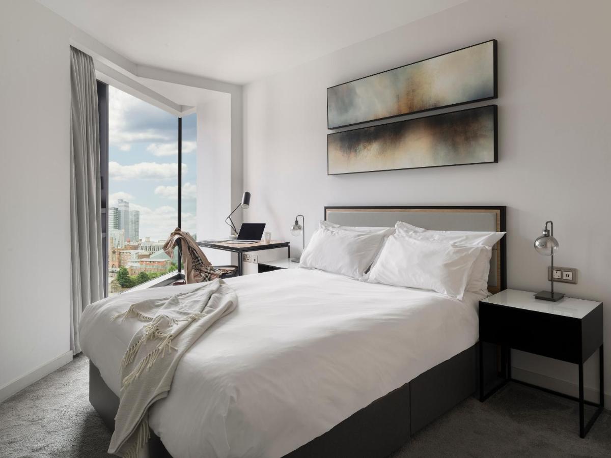 Citysuites Aparthotel Salford  Ngoại thất bức ảnh The photo shows a modern bedroom with a minimalistic design. There's a large bed with white bedding, complemented by decorative pillows. To the side of the bed, there are two nightstands, each with a lamp. A stylish piece of art hangs above the bed, 