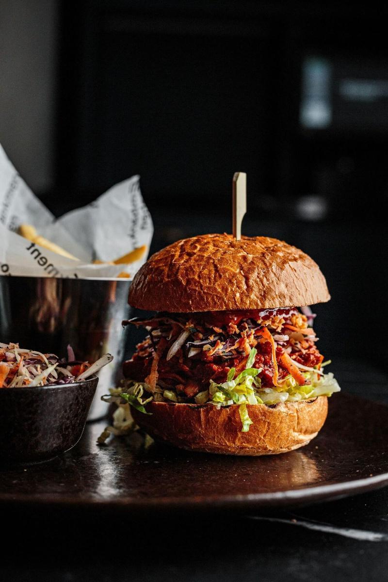 Citysuites Aparthotel Salford  Ngoại thất bức ảnh The photo features a hearty hamburger stacked high with various ingredients. The bun appears to be a toasted, golden-brown color. Inside, there's a generous portion of shredded meat, likely barbecued or pulled. The burger is topped with fresh vegetab