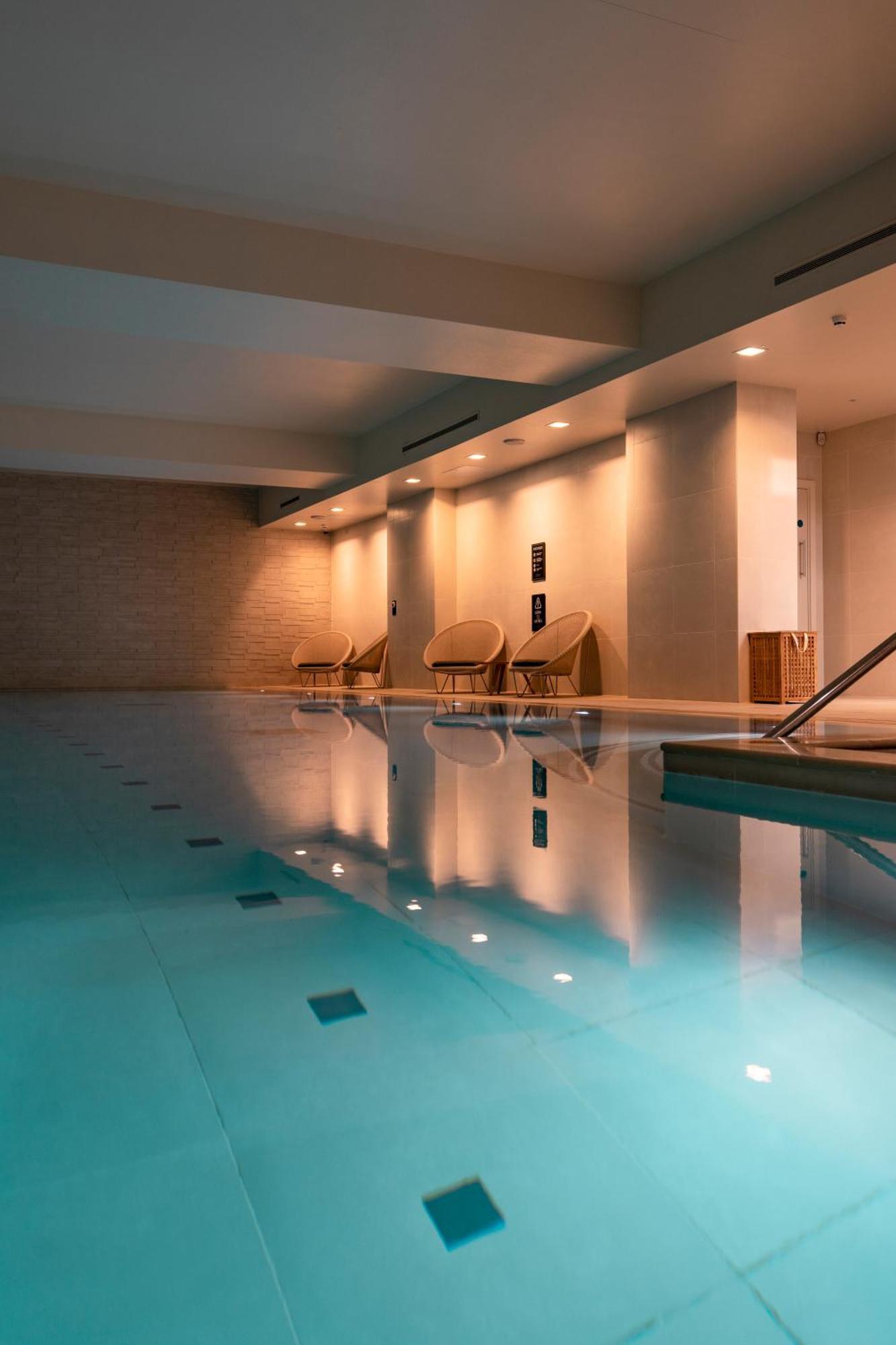 Citysuites Aparthotel Salford  Ngoại thất bức ảnh The photo depicts an indoor swimming pool area. The water is clear and blue, reflecting the soft lighting above. There are several lounge chairs arranged near the pool, providing a relaxing space. The walls are painted in neutral tones, contributing 