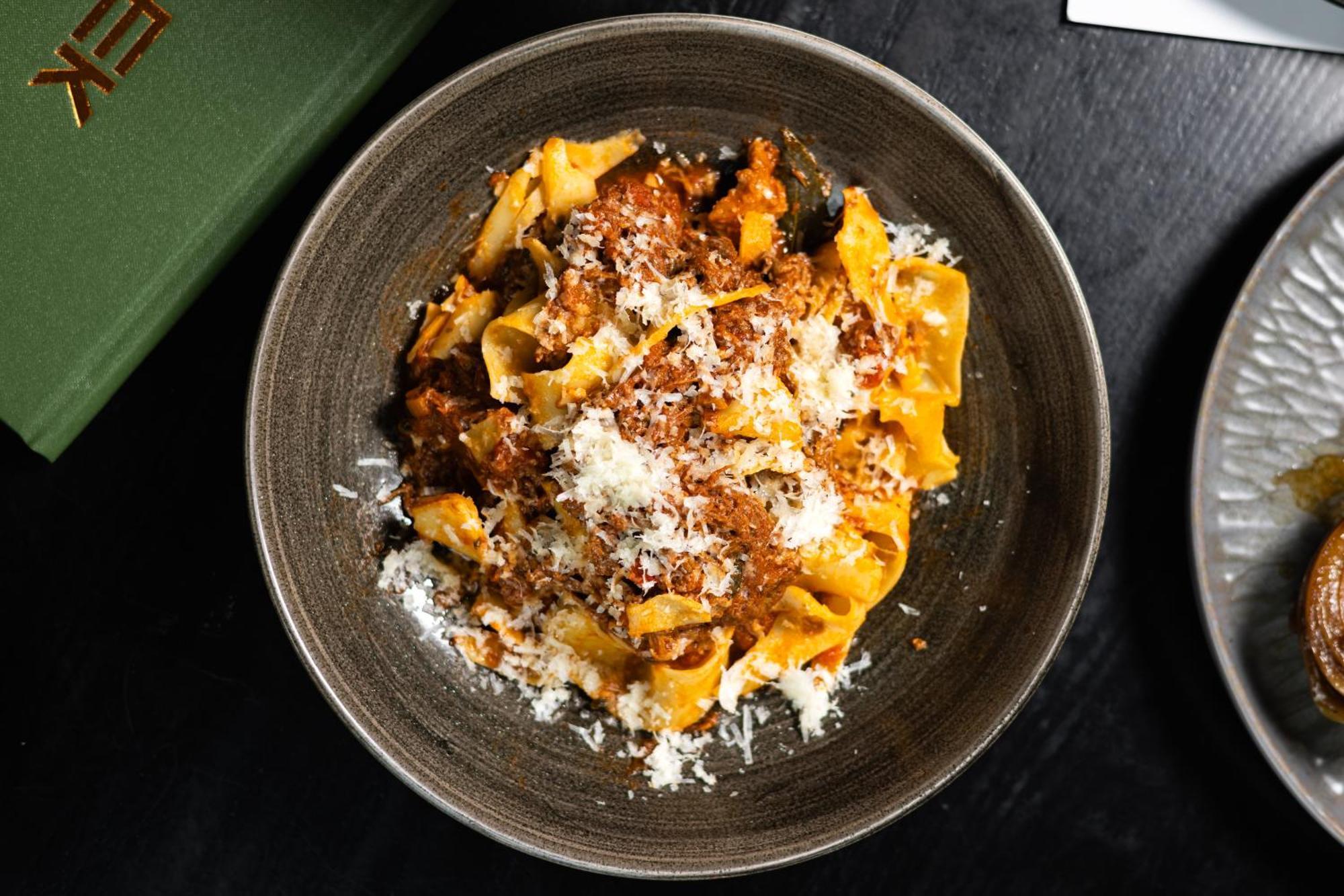 Citysuites Aparthotel Salford  Ngoại thất bức ảnh The photo features a bowl of pasta, likely pappardelle, topped with a rich meat sauce. The dish is garnished with a generous amount of grated cheese, adding a creamy texture to the meal. It's presented in a dark, round bowl, which highlights the vibr