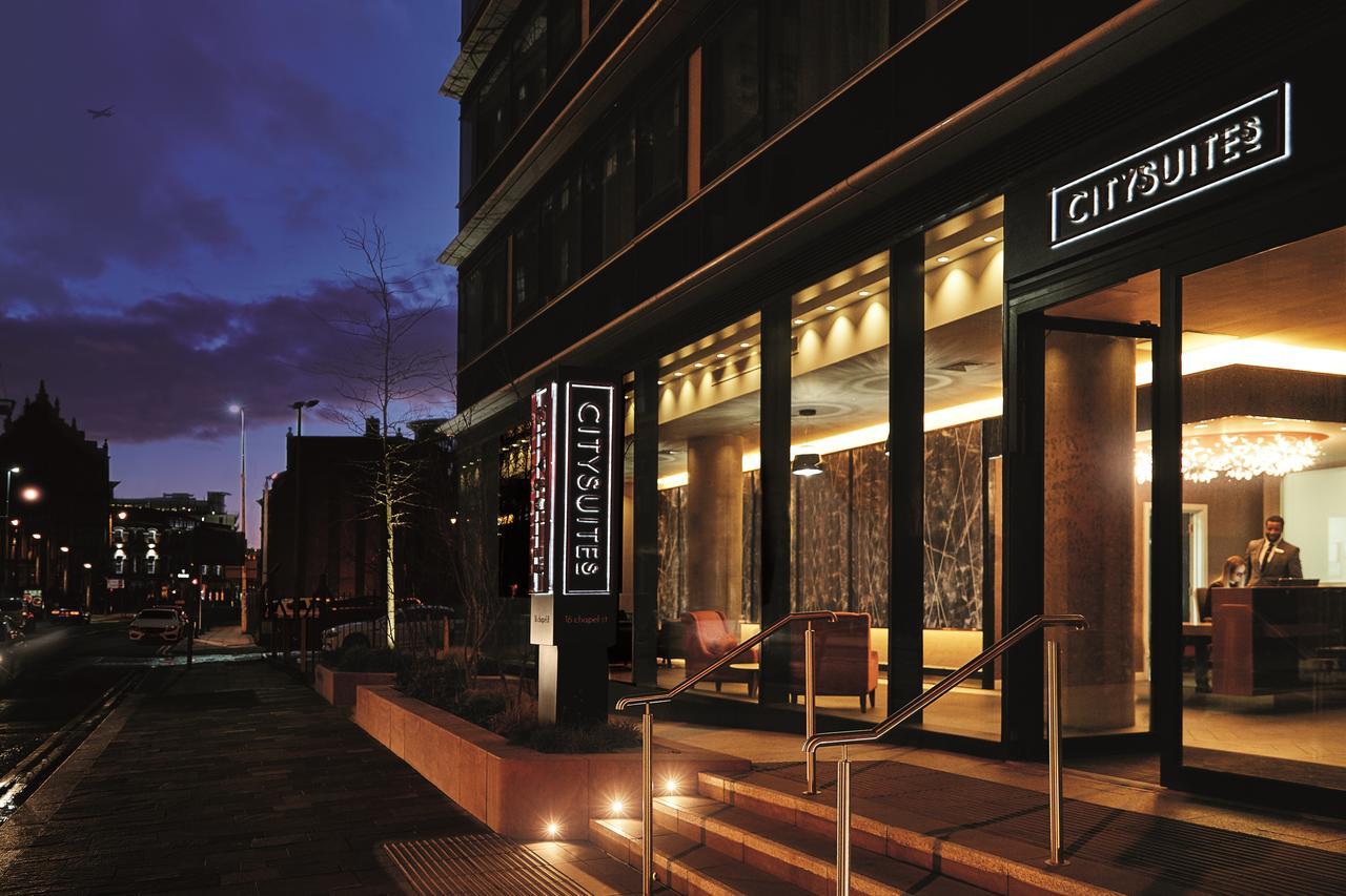 Citysuites Aparthotel Salford  Ngoại thất bức ảnh The photo shows the exterior of a modern hotel named "CitySuites," taken at dusk. The entrance features large glass doors and an illuminated sign displaying the hotel's name. The building has a contemporary design with a sleek facade and warm lightin