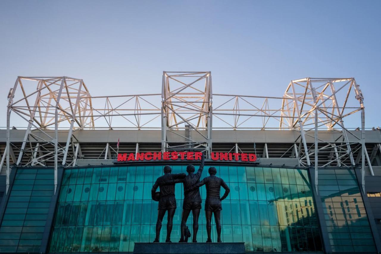 Citysuites Aparthotel Salford  Ngoại thất bức ảnh The photo shows the exterior of Old Trafford, the home stadium of Manchester United Football Club. In front of the stadium, there is a statue depicting three iconic figures from the club's history, known as the "United Trinity." The stadium has a mod