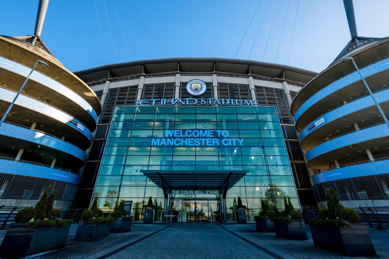 Citysuites Aparthotel Salford  Ngoại thất bức ảnh The image shows the entrance of the Etihad Stadium, which is the home of Manchester City Football Club. The facade features large glass panels with the club's logo prominently displayed at the top. A sign reads "WELCOME TO MANCHESTER CITY." The desig