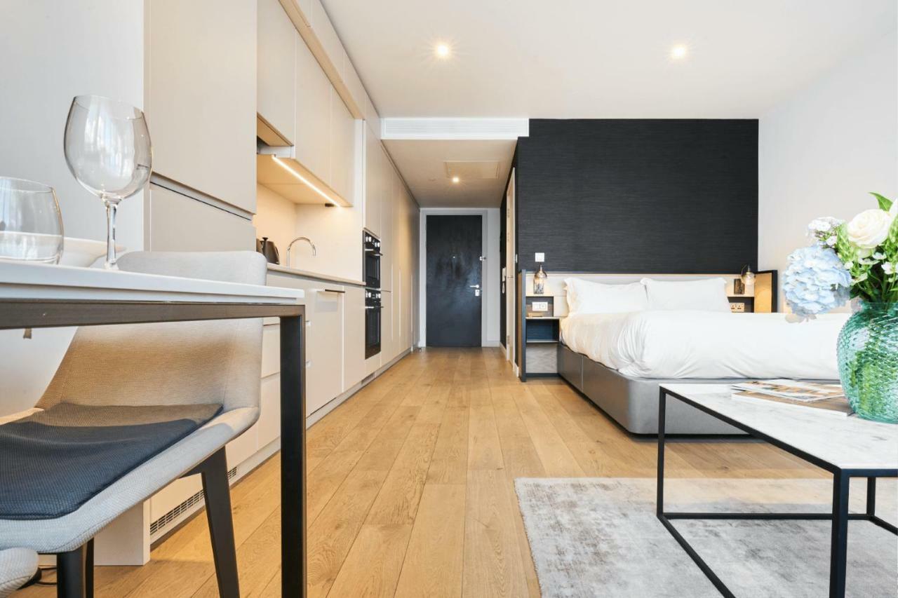 Citysuites Aparthotel Salford  Ngoại thất bức ảnh The photo shows a modern studio apartment. The space features a compact kitchen area with cabinetry and appliances on one side, and a neatly made bed against a dark accent wall. There is a light wooden floor that adds warmth to the room. A small tabl