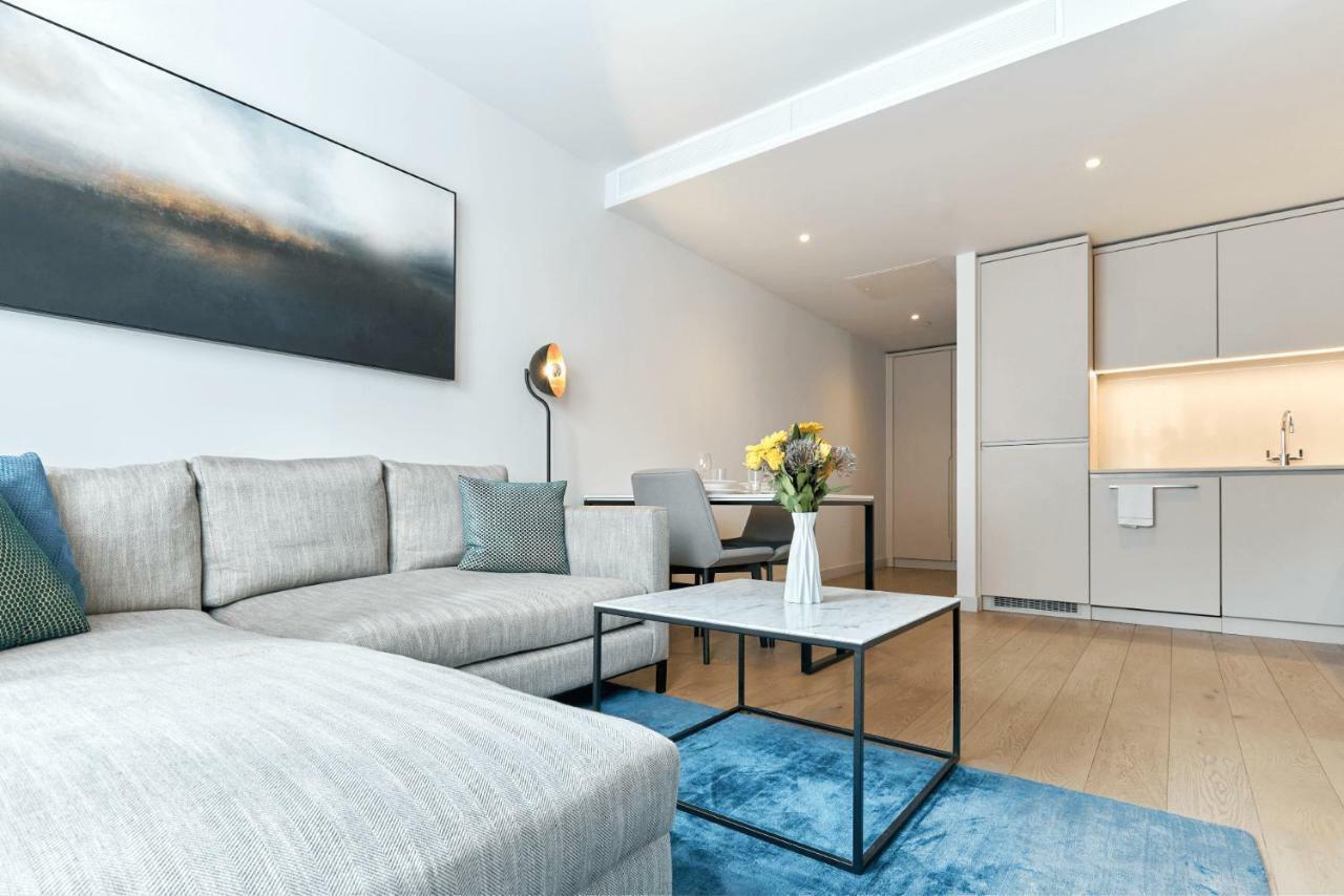 Citysuites Aparthotel Salford  Ngoại thất bức ảnh The photo depicts a modern living space featuring a light-colored sofa with blue and gray throw pillows. In front of the sofa, there is a stylish coffee table with a marble top and a black frame. A vase of fresh flowers adds a touch of color to the t